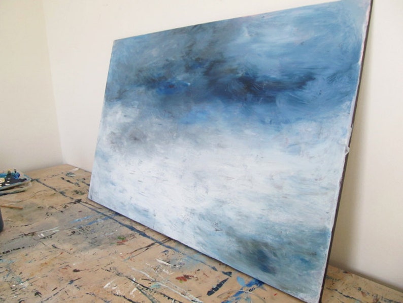 Op de afbeelding: Abstract schilderij op canvas met een blauw en wit kleurenschema. Het schilderij heeft een verloop van blauwe tinten, die naar beneden toe overgaan in een lichter wit. De penseelstreken zijn zichtbaar en cre&euml;ren een textuur effect.