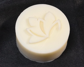 May include: A round, off-white bar of soap featuring a raised, embossed lotus flower design on its top surface. The soap has a smooth, solid texture and a clean, circular shape, presenting a simple and uniform appearance throughout the entire piece.