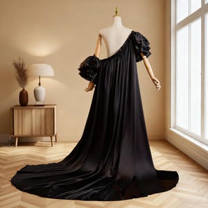 May include: A black, one-shoulder evening gown with a long train. The dress features a ruffled sleeve on one side and is displayed on a mannequin. The fabric appears to be a smooth, flowing material.