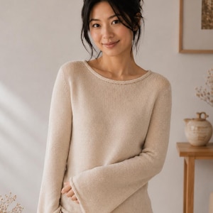 Puede incluir: Un suéter beige de manga larga con un diseño de manga acampanada y un cuello redondo sencillo. La prenda está confeccionada con una textura de punto fino y tiene un dobladillo recto, combinado con pantalones beige a juego con una costura visible.