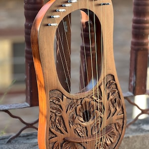 Può includere: Una lira in legno con un design floreale intagliato. La lira ha 10 corde e una tavola armonica in legno. La lira è marrone con una macchia marrone rossiccia.