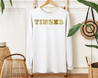 May include: White long-sleeve shirt with the word "YINZER" printed in yellow outlined letters with a colorful pattern inside the letters.