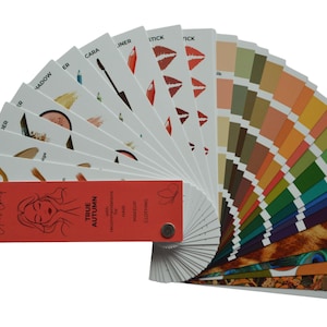 May include: A fan-shaped makeup color palette with various shades of lipstick, eyeshadow, and foundation. The palette includes a red card with the text "Your Colour Chart" and "True Autumn" with a woman's face.