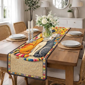 Könnte beinhalten: Ein farbenfroher Tischläufer mit drei stilisierten Katzen in Gelb, Grau und Orange. Die Katzen sind mit Patchwork-Mustern dargestellt und sitzen auf einem beigen Hintergrund. Der Läufer hat einen dekorativen Rand mit einem Mosaikdesign.