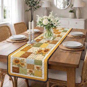 May include: A quilted table runner featuring a sunflower design. The runner has a yellow border and a black stitched edge. The center design includes squares with sunflowers and various colors, including yellow, brown, and green. The runner is placed on a wooden table.