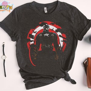 K&ouml;nnte beinhalten: Dunkelgraues T-Shirt mit einem Captain America-Motiv. Das Design zeigt Captain America in einer heldenhaften Pose, vor einem rot-wei&szlig;-blauen Schild. Das T-Shirt hat kurze &Auml;rmel und einen Rundhalsausschnitt.