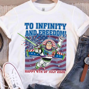 May include: White t-shirt featuring Buzz Lightyear with the text "TO INFINITY AND FREEDOM!" and "HAPPY 4TH OF JULY 2026". The design includes a patriotic color scheme with red, white, and blue elements, and fireworks.