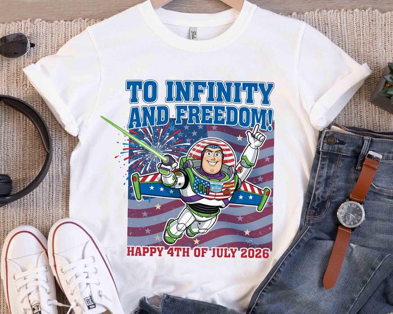 May include: White t-shirt featuring Buzz Lightyear with the text "TO INFINITY AND FREEDOM!" and "HAPPY 4TH OF JULY 2026". The design includes a patriotic color scheme with red, white, and blue elements, and fireworks.