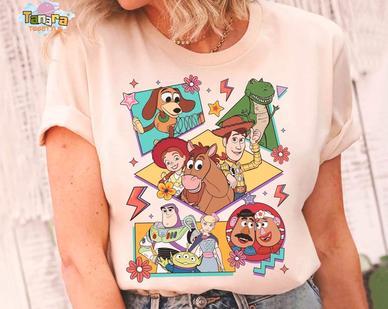 Peut inclure: T-shirt cr&egrave;me avec un graphisme color&eacute; des personnages du film d'animation "Toy Story". Le motif comprend des images de Woody, Buzz l'&Eacute;clair et d'autres personnages, avec des &eacute;toiles, des fleurs et des &eacute;clairs d&eacute;coratifs.