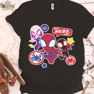 May include: Black t-shirt featuring a colorful graphic of Spider-Man characters. The design includes Spider-Gwen, Spider-Man, and Miles Morales, with the text "GO-WEBS-GO!". The graphic is surrounded by spider web and star accents.