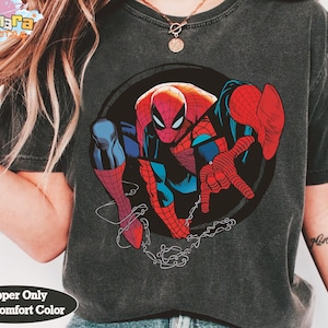 May include: Dark gray t-shirt featuring a large graphic of Spider-Man in a dynamic pose. The superhero is depicted in his classic red and blue suit, with a black circle background. The shirt has the text "Pepper Only With Comfort Color".