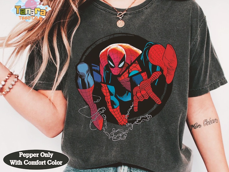 May include: Dark gray t-shirt featuring a large graphic of Spider-Man in a dynamic pose. The superhero is depicted in his classic red and blue suit, with a black circle background. The shirt has the text "Pepper Only With Comfort Color".