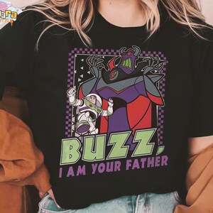 May include: Black t-shirt with a graphic of Buzz Lightyear and Zurg from Toy Story. The design includes the text "BUZZ. I AM YOUR FATHER" in green and white. The image has a purple and black checkered border.