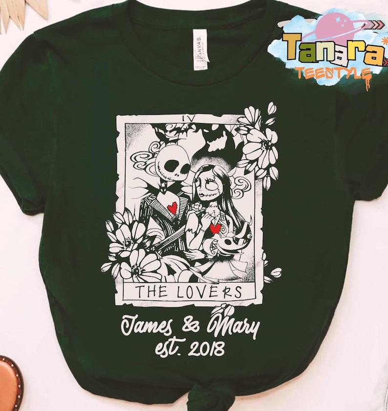 May include: Dark green t-shirt featuring a black and white illustration of Jack and Sally from The Nightmare Before Christmas, with the text "THE LOVERS" and "James & Mary est. 2018". The design is framed by floral elements.