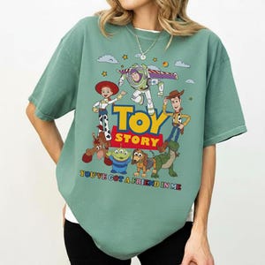 Puede incluir: Camiseta verde salvia con un gr&aacute;fico colorido de personajes de la pel&iacute;cula "Toy Story". El dise&ntilde;o incluye a Woody, Buzz Lightyear, Jessie y otros personajes, con las palabras "Toy Story" y "You've Got a Friend in Me."