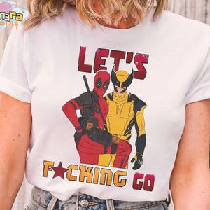 Puede incluir: Camiseta blanca con un gr&aacute;fico de Deadpool y Lobezno y el texto "LET'S F*CKING GO" en rojo y naranja. El dise&ntilde;o incluye el logotipo de Tanara TeeStyle.