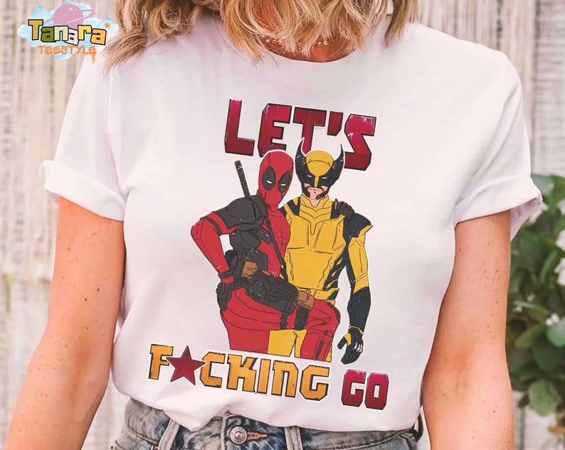 Puede incluir: Camiseta blanca con un gr&aacute;fico de Deadpool y Lobezno y el texto "LET'S F*CKING GO" en rojo y naranja. El dise&ntilde;o incluye el logotipo de Tanara TeeStyle.