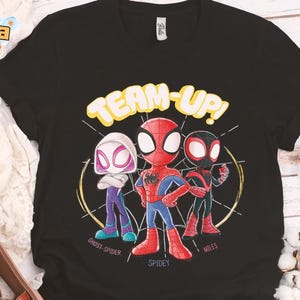 May include: Black t-shirt featuring a cartoon graphic of Spider-Man, Spider-Gwen, and Miles Morales with the words "TEAM-UP!". The characters are in their superhero costumes, with the names "Ghost-Spider", "Spidey", and "Miles" below them.