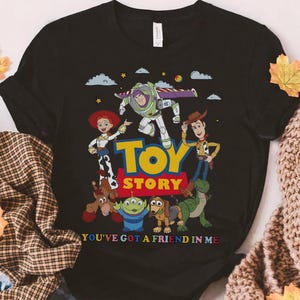 Puede incluir: Camiseta negra con un gr&aacute;fico colorido de personajes de la pel&iacute;cula animada "Toy Story". El dise&ntilde;o incluye a Buzz Lightyear, Woody, Jessie y otros personajes, con las palabras "Toy Story" y "You've Got a Friend in Me."
