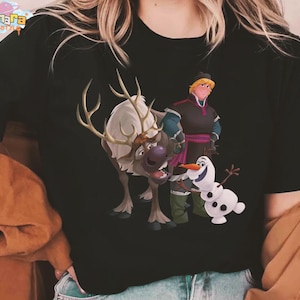 Peut inclure: T-shirt noir avec un graphisme color&eacute; des personnages du film d'animation La Reine des Neiges. Le motif comprend Kristoff, Olaf le bonhomme de neige et Sven le renne. Le t-shirt porte le texte "Tanara Teeshirts" en haut.