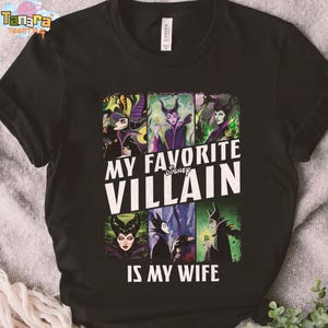 May include: Black t-shirt featuring a graphic with the text "MY FAVORITE VILLAIN IS MY WIFE" and images of Disney villains. The design includes images of Maleficent, the Evil Queen, and other iconic characters. The shirt is made of a soft material.