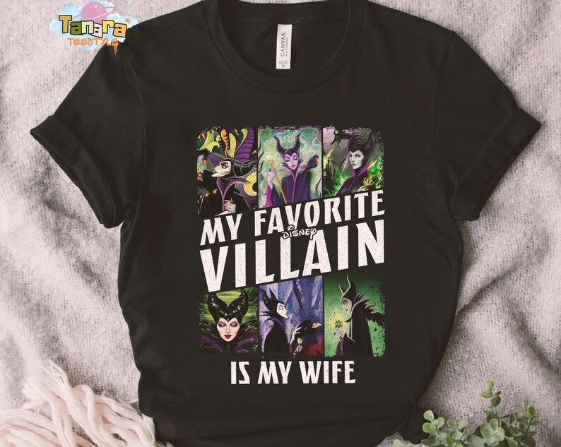 May include: Black t-shirt featuring a graphic with the text "MY FAVORITE VILLAIN IS MY WIFE" and images of Disney villains. The design includes images of Maleficent, the Evil Queen, and other iconic characters. The shirt is made of a soft material.