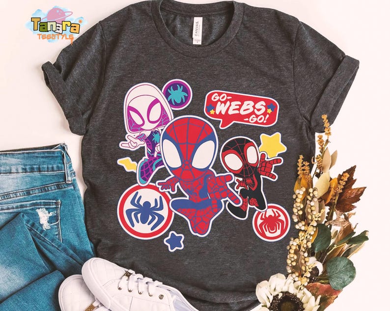 May include: Dark gray t-shirt featuring cartoon illustrations of Spider-Man characters. The design includes Spider-Gwen, Spider-Man, and Miles Morales, with the text "GO-WEBS-GO!" in a speech bubble. Additional spider web and star graphics are also present.