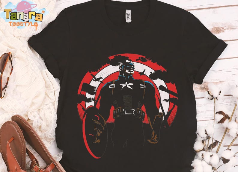 K&ouml;nnte beinhalten: Schwarzes T-Shirt mit Captain America-Grafik. Das Design zeigt einen Schild, einen Stern und den Text "Tanara Teenstyle". Die Grafik ist in Rot, Wei&szlig; und Blau gehalten.