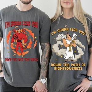 May include: Two charcoal gray t-shirts with matching graphics. One features a red devil with the text "I'M GONNA LEAD YOU DOWN THE PATH THAT ROCKS." The other shows an angel with the text "I'M GONNA LEAD YOU DOWN THE PATH OF RIGHTEOUSNESS."