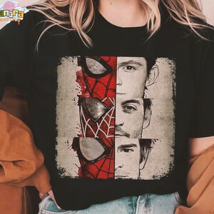 Puede incluir: Camiseta negra con un dise&ntilde;o gr&aacute;fico de tres caras de Spider-Man, cada una representando a un actor diferente. El dise&ntilde;o incluye la m&aacute;scara de Spider-Man en rojo y negro, con las caras de los actores en escala de grises. La camiseta tiene el texto "Tanara Tees".