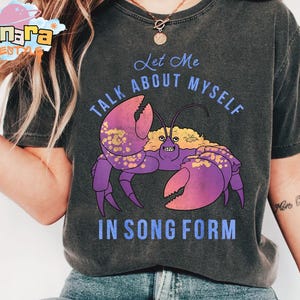 Puede incluir: Camiseta gris oscuro con una ilustraci&oacute;n de cangrejo morado con pinzas rosas y el texto "Let Me Talk About Myself In Song Form". La camiseta tiene un aspecto vintage descolorido.
