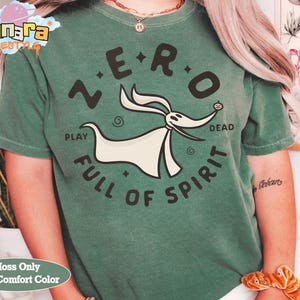 Puede incluir: Una camiseta verde musgo con un gr&aacute;fico de Zero de The Nightmare Before Christmas. El dise&ntilde;o incluye el texto "ZERO" encima del personaje y "PLAY FULL OF SPIRIT" debajo. La camiseta tiene cuello redondo y mangas cortas.