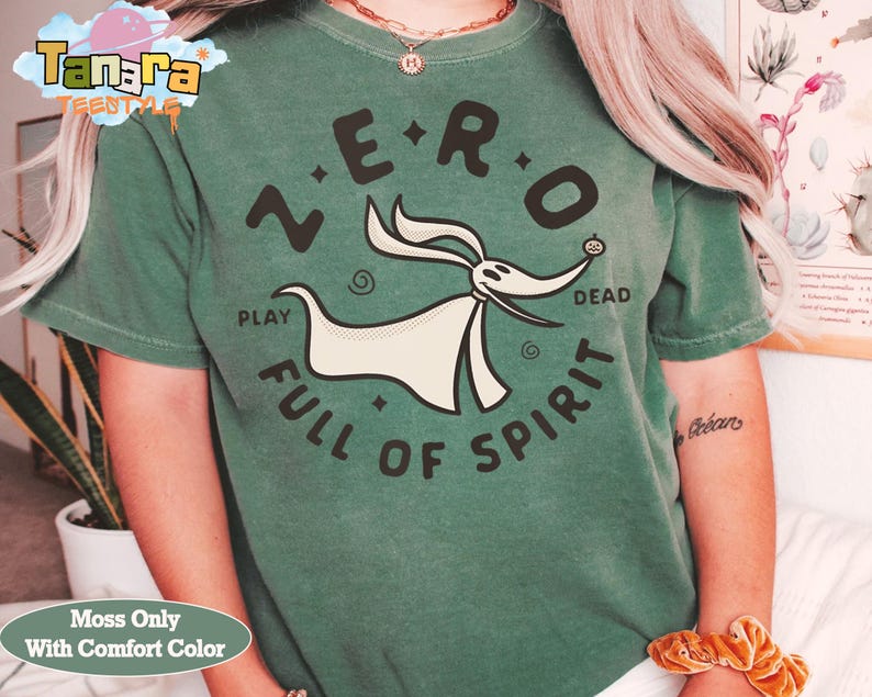 Puede incluir: Una camiseta verde musgo con un gr&aacute;fico de Zero de The Nightmare Before Christmas. El dise&ntilde;o incluye el texto "ZERO" encima del personaje y "PLAY FULL OF SPIRIT" debajo. La camiseta tiene cuello redondo y mangas cortas.