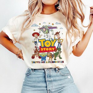 Puede incluir: Camiseta color crema con un gr&aacute;fico colorido de personajes de la pel&iacute;cula "Toy Story". El dise&ntilde;o incluye las palabras "Toy Story" en amarillo y la frase "You've Got a Friend in Me".