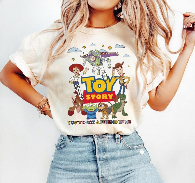 Puede incluir: Camiseta color crema con un gr&aacute;fico colorido de personajes de la pel&iacute;cula "Toy Story". El dise&ntilde;o incluye las palabras "Toy Story" en amarillo y la frase "You've Got a Friend in Me".
