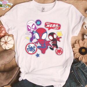 May include: White t-shirt featuring colorful cartoon graphics of Spider-Man characters. The design includes the text "GO WEBS - GO!" and various spider-themed emblems. The shirt is styled with a knot at the bottom.