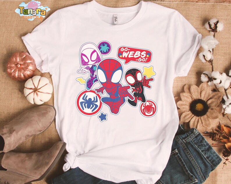 May include: White t-shirt featuring colorful cartoon graphics of Spider-Man characters. The design includes the text "GO WEBS - GO!" and various spider-themed emblems. The shirt is styled with a knot at the bottom.