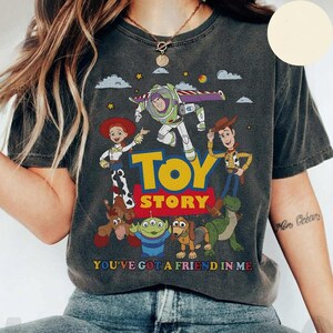 Puede incluir: Camiseta gris oscuro con un dise&ntilde;o colorido de Toy Story. Presenta a Buzz Lightyear, Woody y Jessie, con la inscripci&oacute;n "TOY STORY" en amarillo. La frase "YOU'VE GOT A FRIEND IN ME" tambi&eacute;n est&aacute; presente.
