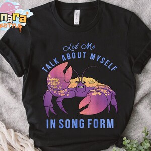 Puede incluir: Camiseta negra con una ilustraci&oacute;n de un cangrejo de dibujos animados. El cangrejo es morado y rosa con detalles dorados. El texto de la camiseta dice "Let Me Talk About Myself In Song Form" en azul. La camiseta es de material suave.