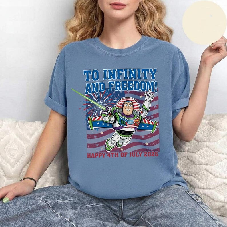 May include: A light blue t-shirt featuring Buzz Lightyear with the text "TO INFINITY AND FREEDOM!" and "HAPPY 4TH OF JULY 2026" in red. The design includes a red, white, and blue American flag and fireworks.