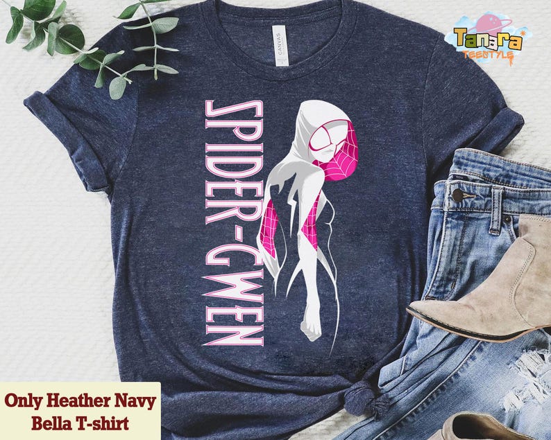 May include: Heather navy Bella T-shirt featuring a Spider-Gwen graphic. The design includes a white and pink illustration of the character with the text "SPIDER-GWEN" in pink. The shirt is paired with blue jeans and a beige boot.