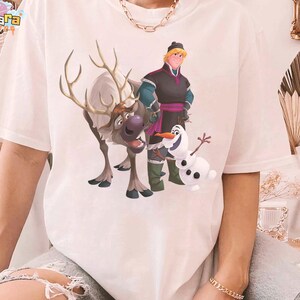 Peut inclure: T-shirt blanc avec une illustration color&eacute;e des personnages du film d'animation La Reine des Neiges : Kristoff, Sven le renne et Olaf le bonhomme de neige. Le motif est centr&eacute; sur le devant.