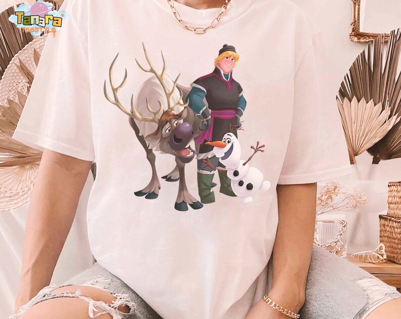 Peut inclure: T-shirt blanc avec une illustration color&eacute;e des personnages du film d'animation La Reine des Neiges : Kristoff, Sven le renne et Olaf le bonhomme de neige. Le motif est centr&eacute; sur le devant.