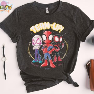 May include: Dark gray t-shirt featuring a graphic of three cartoon Spider-Man characters with the words "TEAM-UP!". The characters include Ghost-Spider, Spidey, and Miles, each in their signature colors.