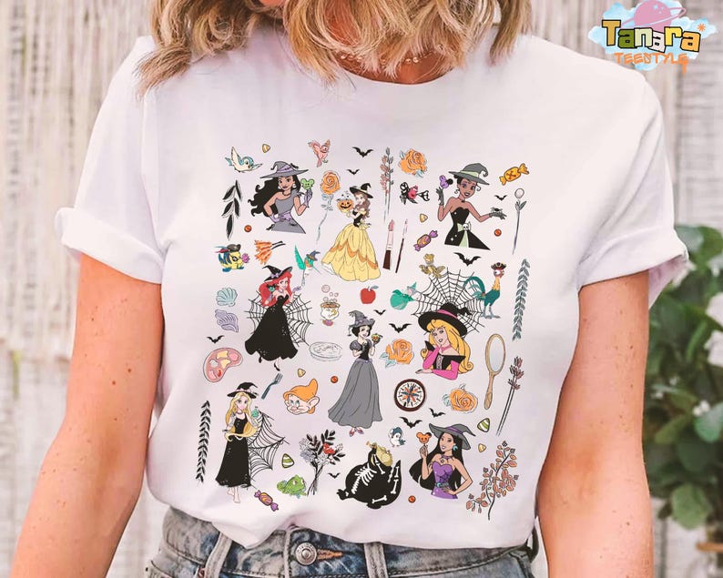 May include: White t-shirt featuring a colorful Halloween-themed graphic. The design includes illustrations of witches, bats, roses, and other spooky elements. The text "Tanara Teestyles" is printed on the top right corner.