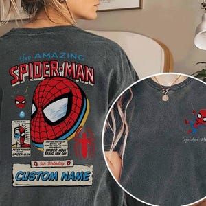 Puede incluir: Camiseta gris con un dise&ntilde;o de Spider-Man. La parte trasera presenta un gran gr&aacute;fico de Spider-Man con el texto "the AMAZING SPIDER-MAN" y "CUSTOM NAME". Un gr&aacute;fico m&aacute;s peque&ntilde;o de Spider-Man est&aacute; en la parte delantera de la camiseta.