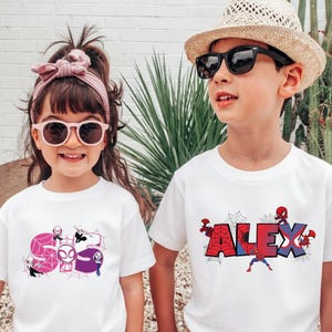 Puede incluir: Dos ni&ntilde;os con camisetas blancas con dise&ntilde;os de superh&eacute;roes. Una camiseta presenta el nombre "ALEX" con un tema de Spider-Man, mientras que la otra muestra "Gwen Stacy" con un dise&ntilde;o de telara&ntilde;a. Ambos llevan gafas de sol.