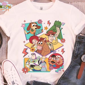 Peut inclure: T-shirt blanc avec un graphisme color&eacute; des personnages de Toy Story. Le design pr&eacute;sente Woody, Buzz Lightyear, Rex et d'autres personnages dans un style r&eacute;tro. Le t-shirt est fait d'une mati&egrave;re douce.