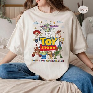Puede incluir: Camiseta de color marfil con un gr&aacute;fico colorido de los personajes de Toy Story, incluyendo a Woody, Buzz Lightyear y Jessie. Las palabras "TOY STORY" est&aacute;n en letras grandes y en negrita, con la frase "YOU'VE GOT A FRIEND IN ME" debajo.