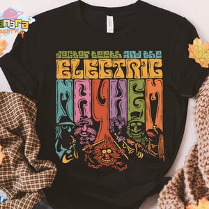 May include: Black t-shirt featuring a colorful graphic of Dr. Teeth and the Electric Mayhem band. The design includes the band's name in a retro font and images of the Muppet characters. The shirt has a classic crew neck and short sleeves.